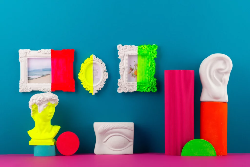 Un'esposizione artistica con dei quadri e delle cornici classiche colorate a metà, con delle statue e degli elementi atratti su sfondo azzurro